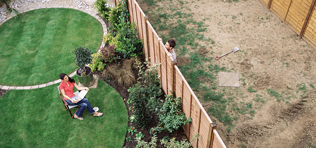 man in empty block looking over fence at nice garden